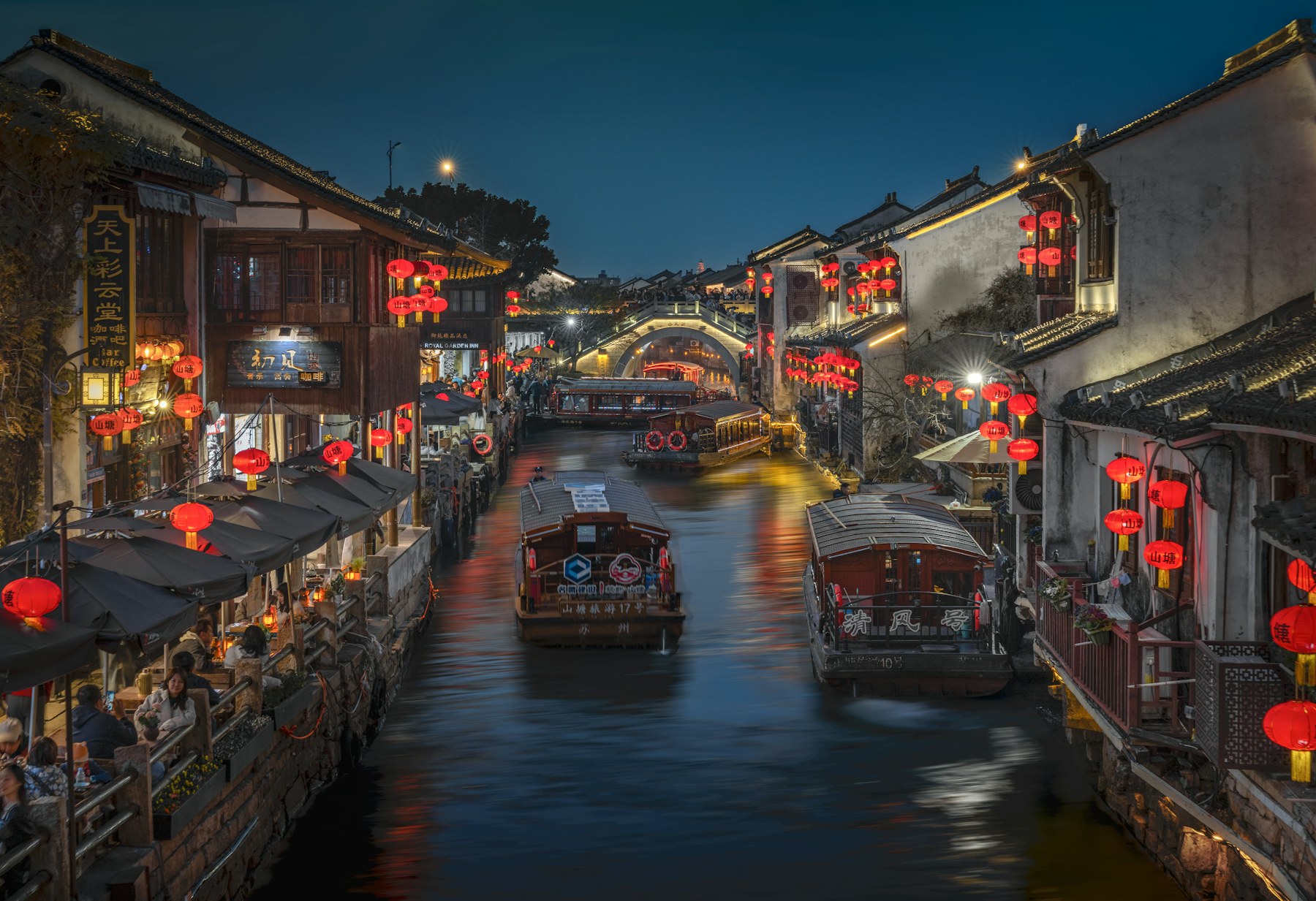 Red lanterns, traditional boats and warm reflections along a canal in Suzhou at night